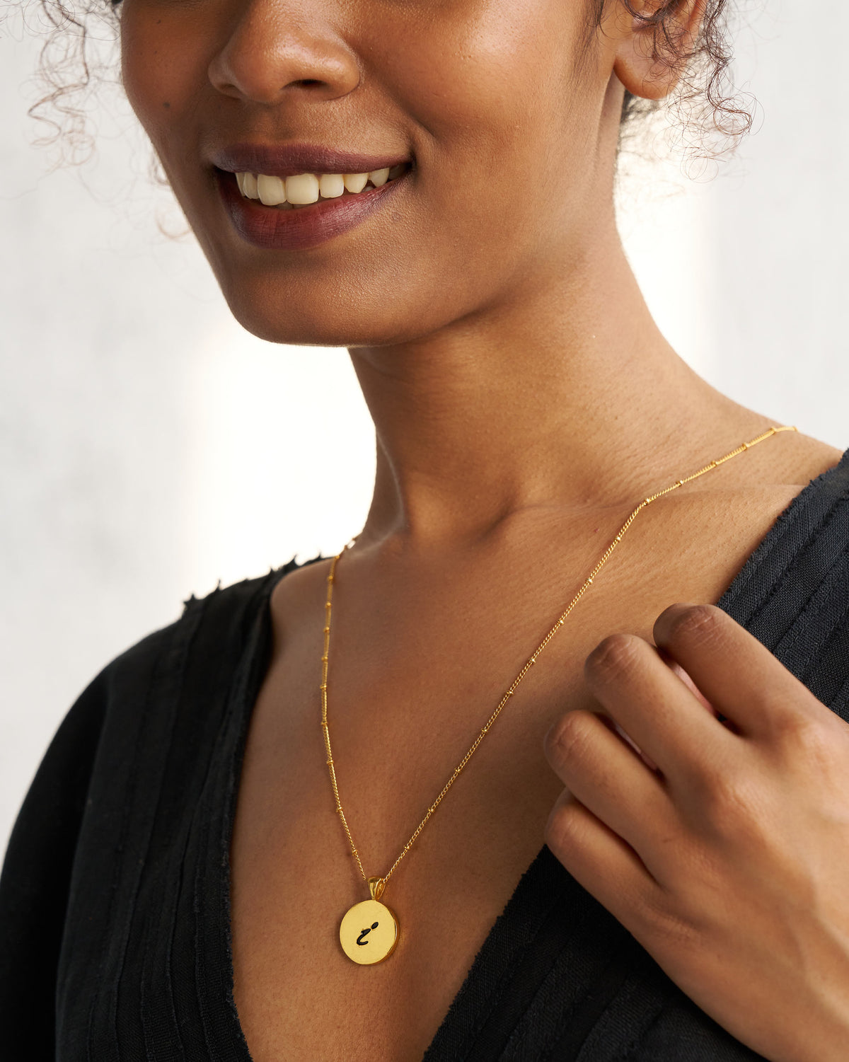 Gold Alphabet I charm with a black script letter i when worn.