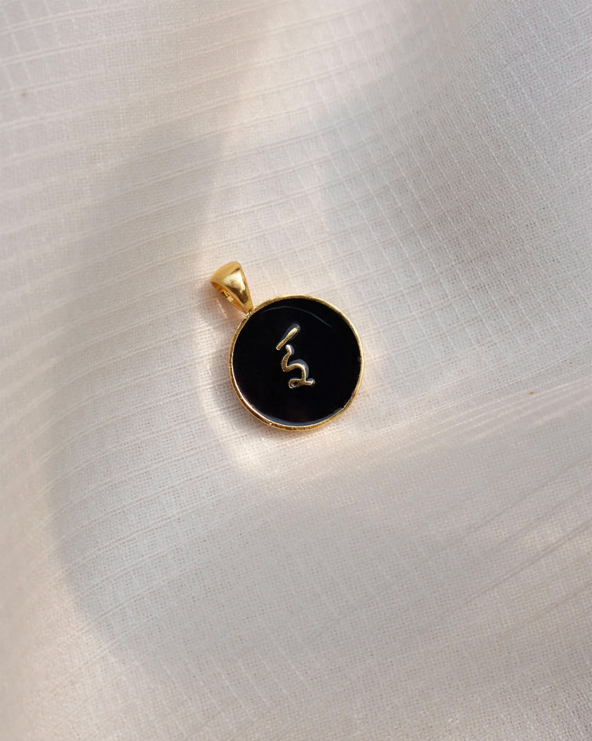 Close-up of a black and gold Alphabet I charm showing इ.