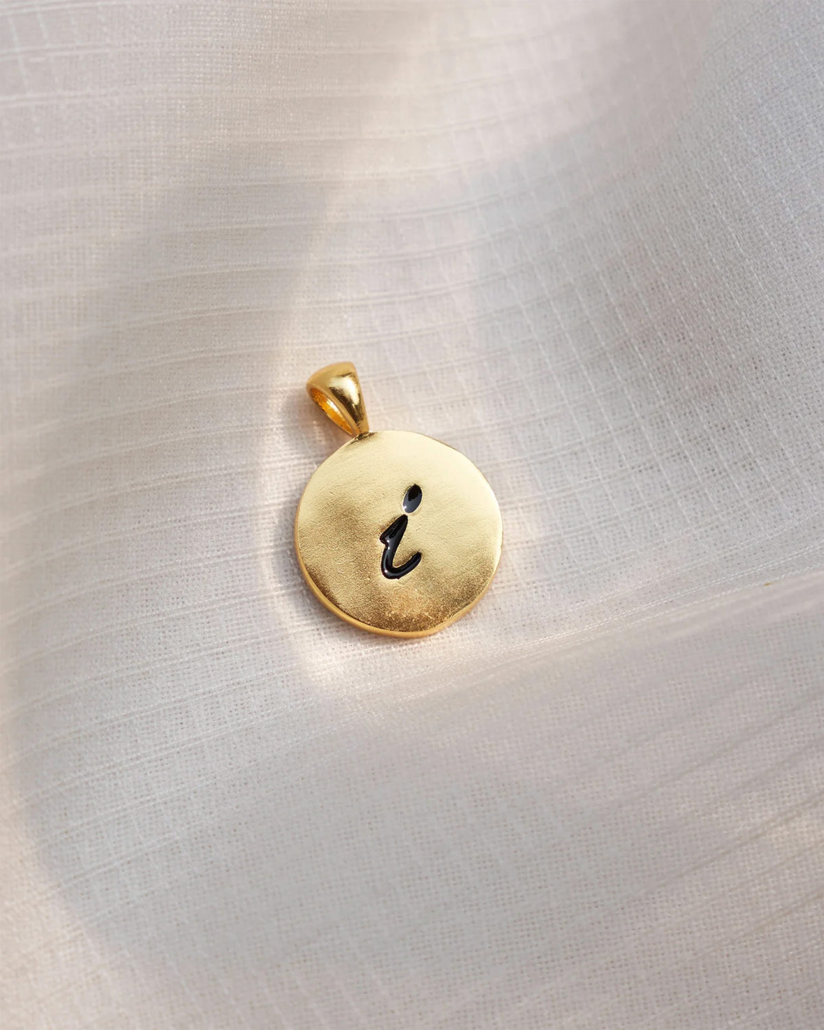 Close-up of a gold Alphabet I charm with a black script i.