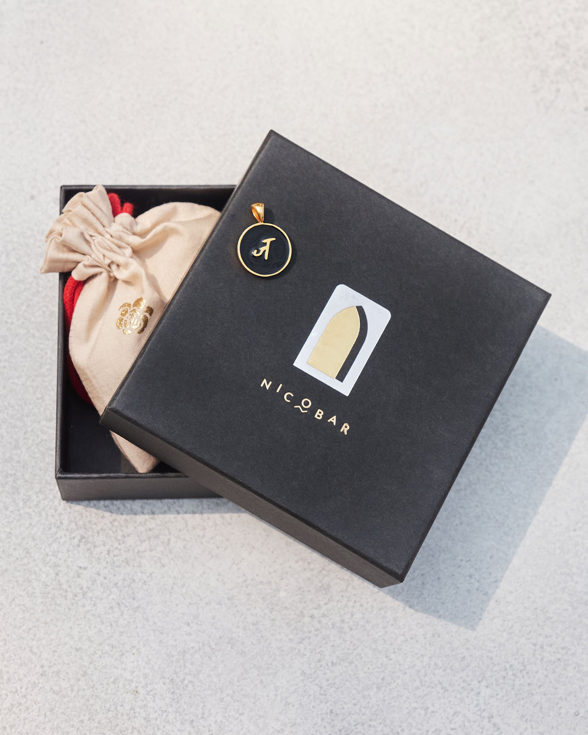 Black and gold Alphabet J charm with ज on a Nicobar gift box.