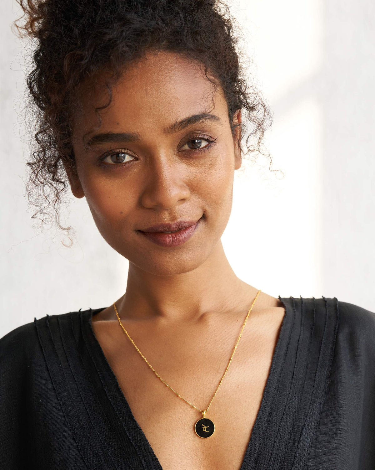 Person wearing a black and gold alphabet charm necklace.