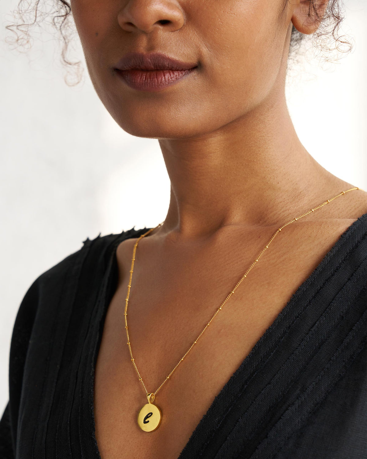 Gold alphabet charm with a black script letter worn on a fine chain.