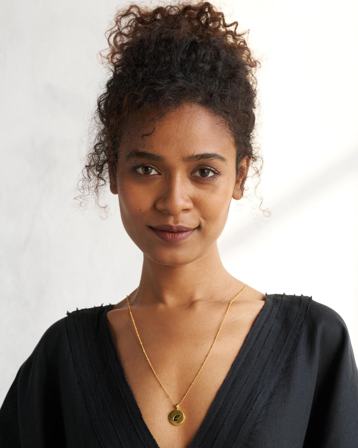 Alphabet E charm worn on a gold chain with a black V-neck top.