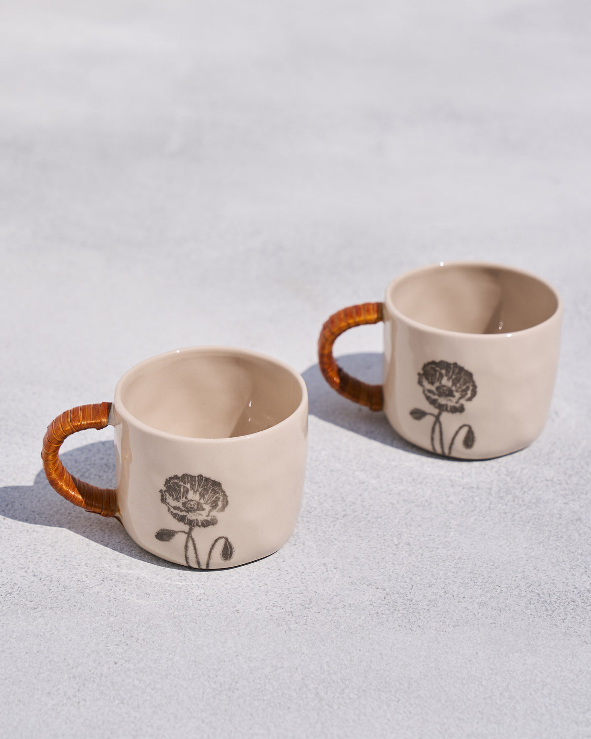 Poppy mugs with rattan handles showing black poppy line drawings.