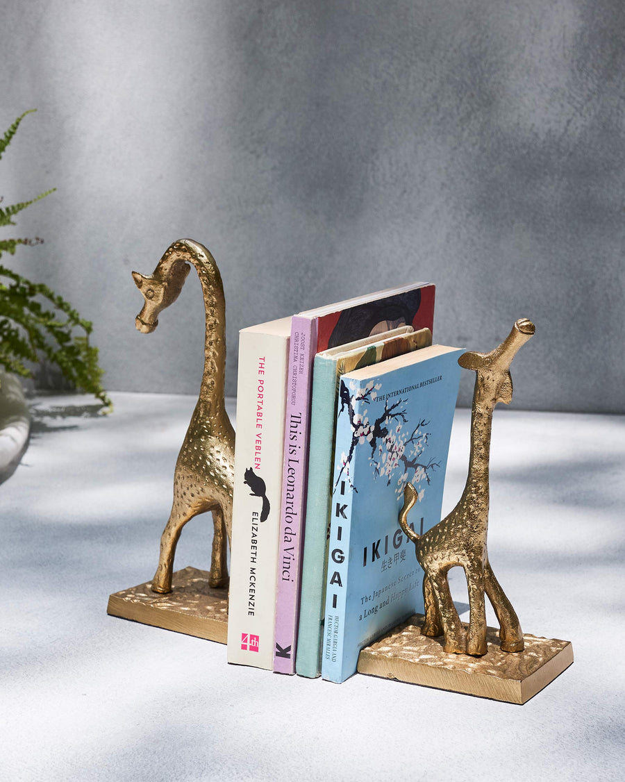 Two gold giraffe bookends holding a stack of books