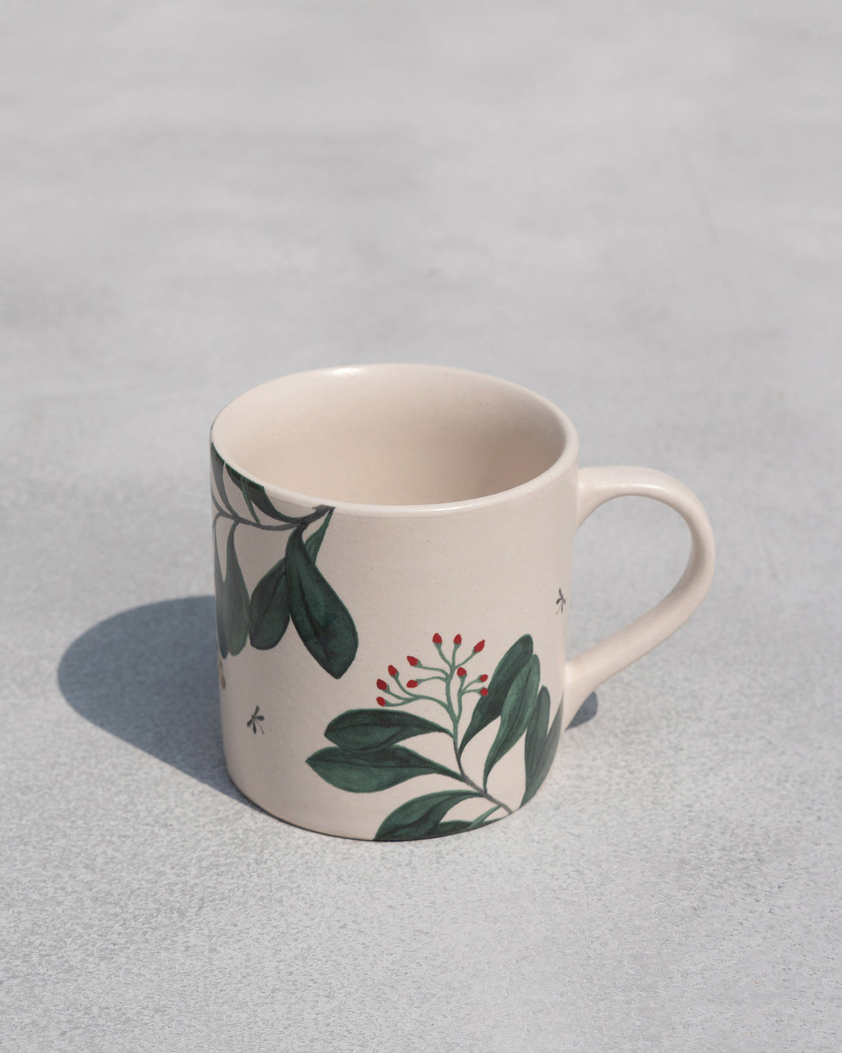 Side view of a Zuri Straight Mug with a handle on the right and painted leaves.