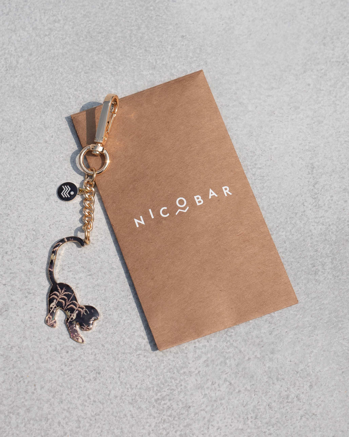 Monkey keychain with gold palm motifs beside a Nicobar card.