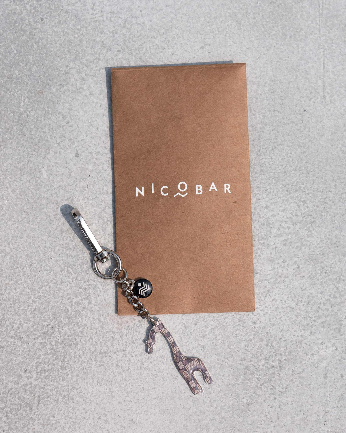 Giraffe Keychain placed on a kraft card printed with the Nicobar logo.