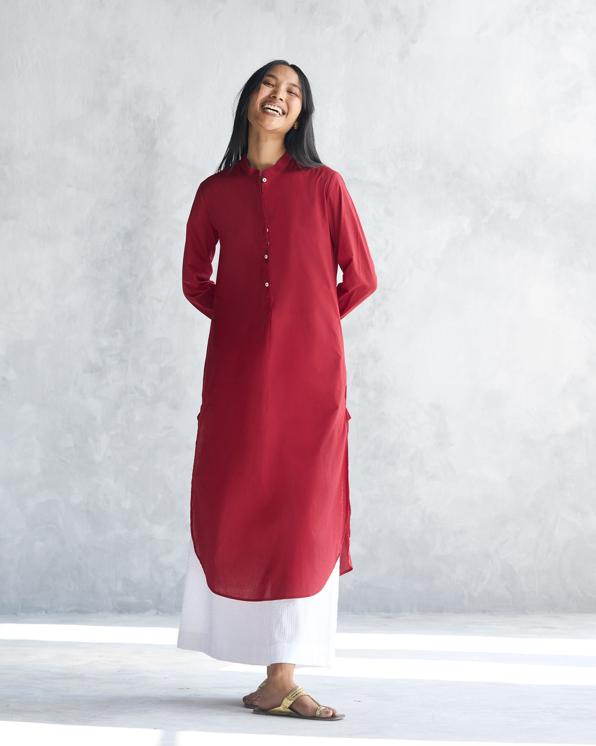 Person wearing a red long kurta with side slits and a curved hem.