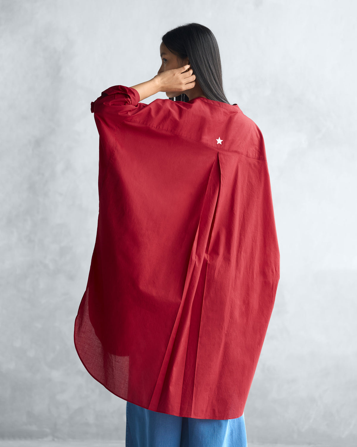 Back of a red Lazy Sunday tunic with a box pleat and white embroidered star.