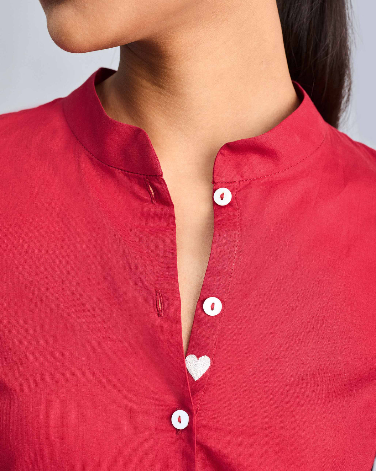 Close-up of a red mandarin collar placket with a white heart embroidery.