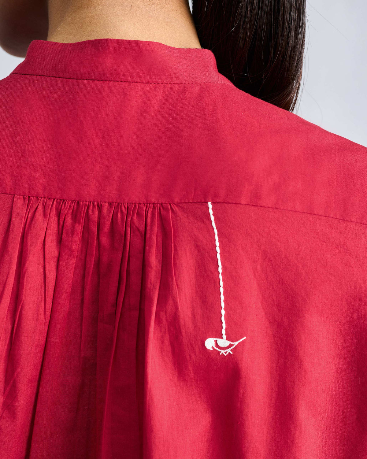 Close-up of white bird embroidery on the back of a red mandarin collar top.