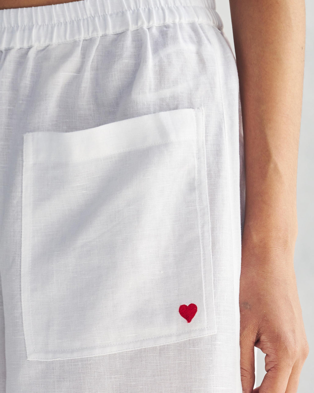 Close-up of white Serene pants showing a red embroidered heart on the patch pocket.