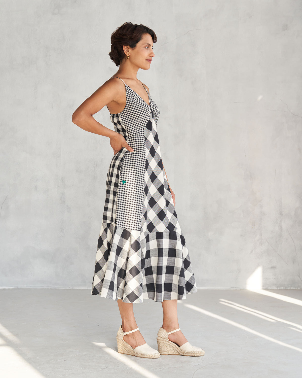 Side view of an ivory and black check strappy midi dress with a tiered hem.