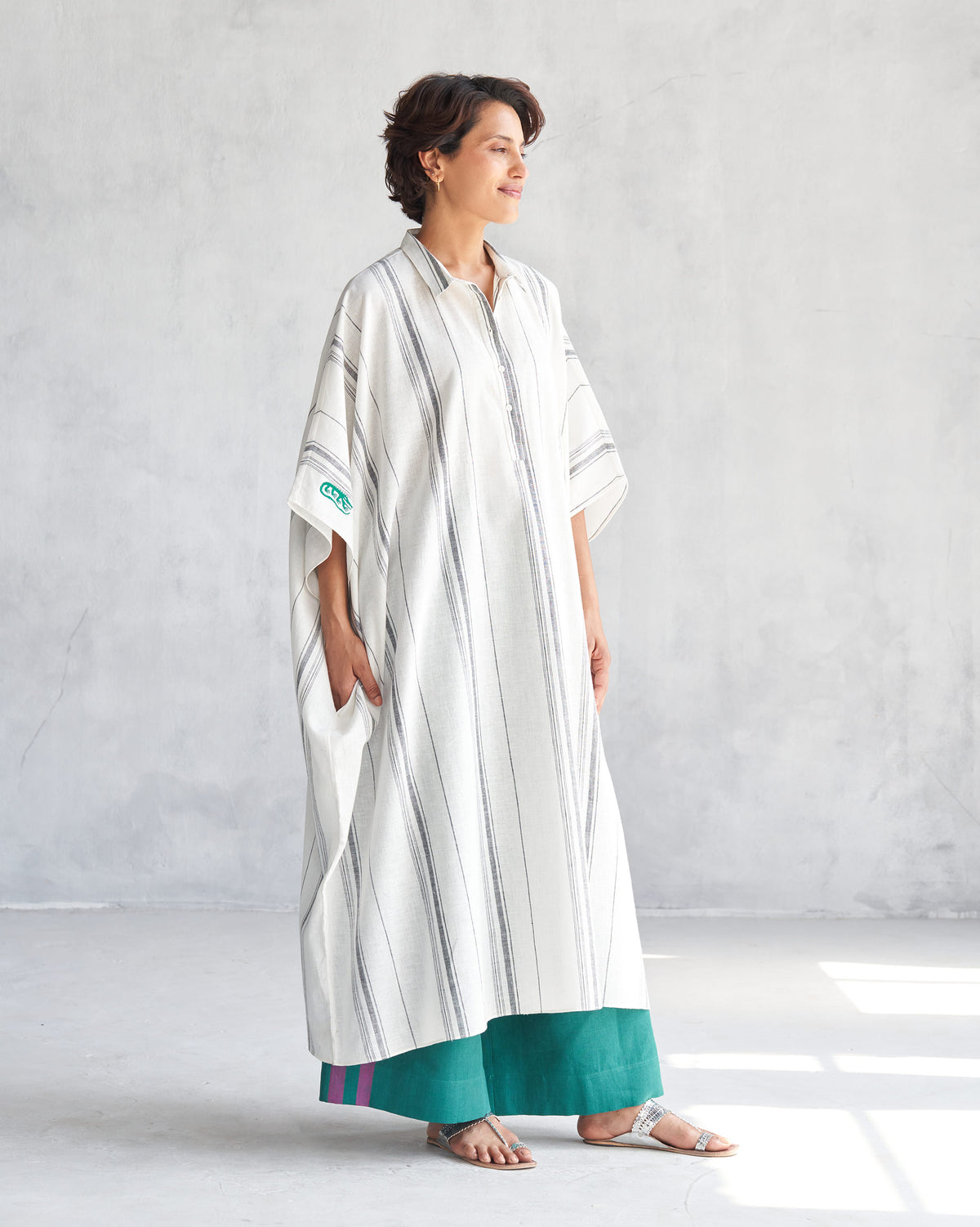 Side view of an ivory collared kaftan with grey stripes and a side pocket.