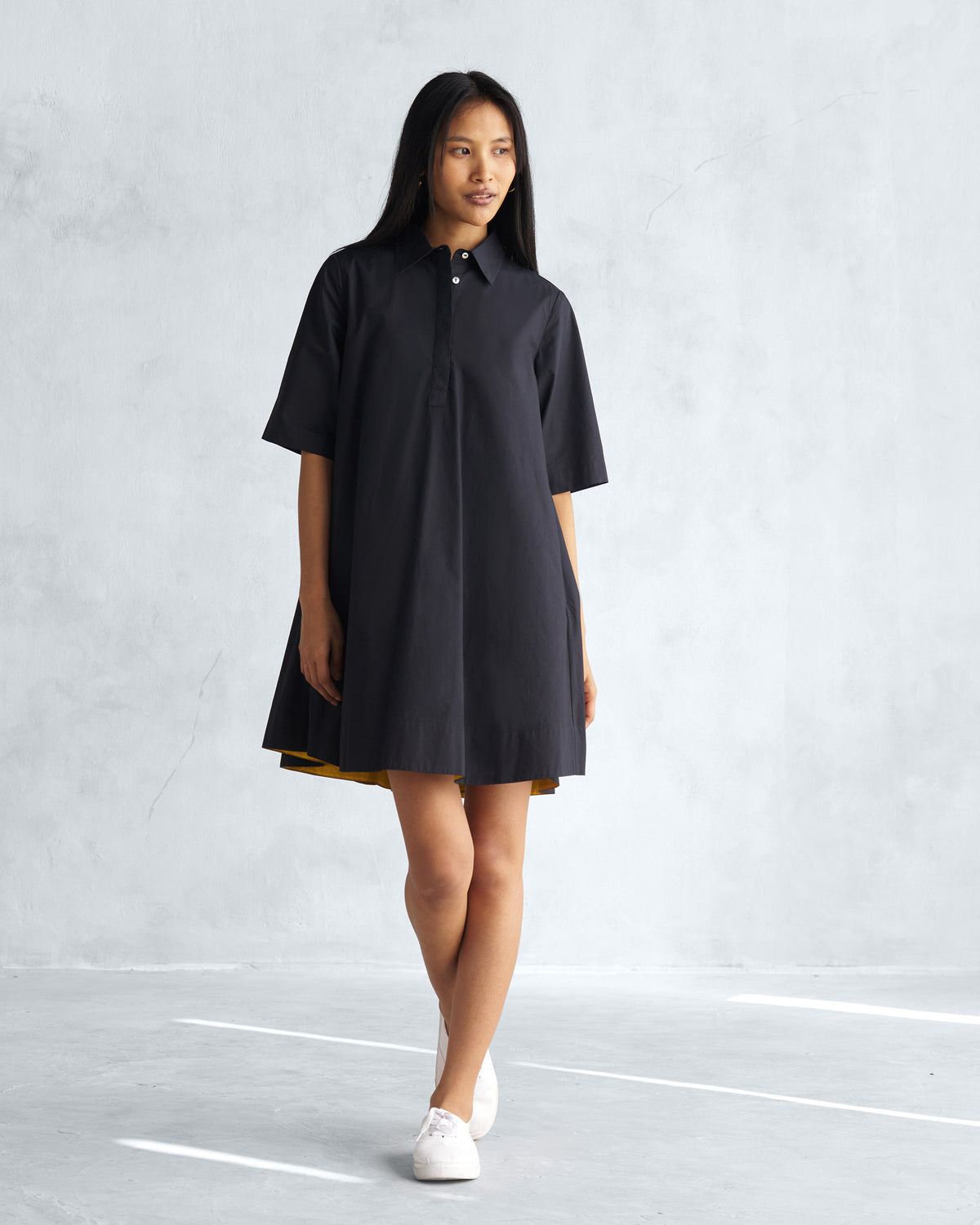 Person wearing a black A-line short dress with a shirt collar.