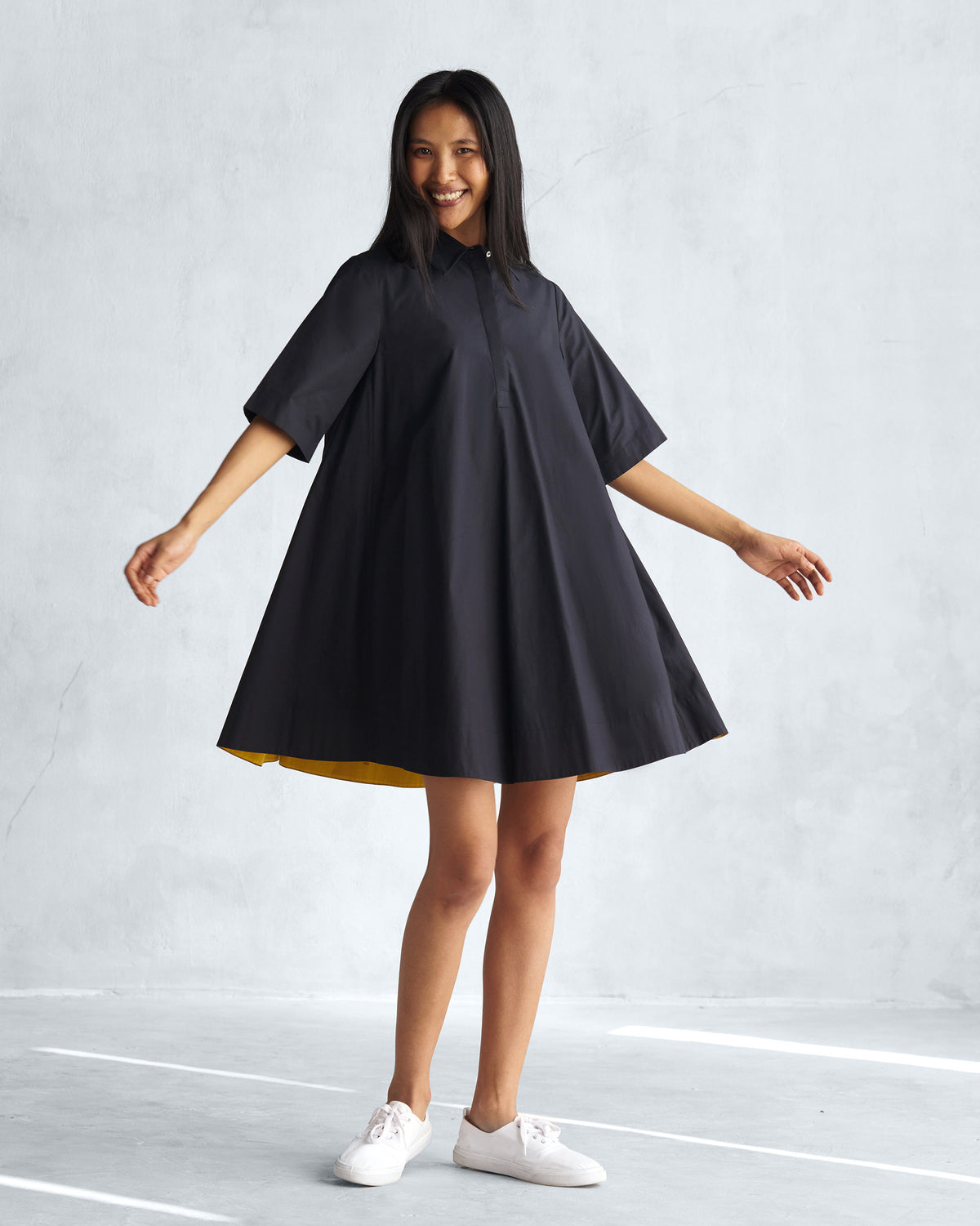 Person wearing a black A-line short dress with yellow lining at the hem.