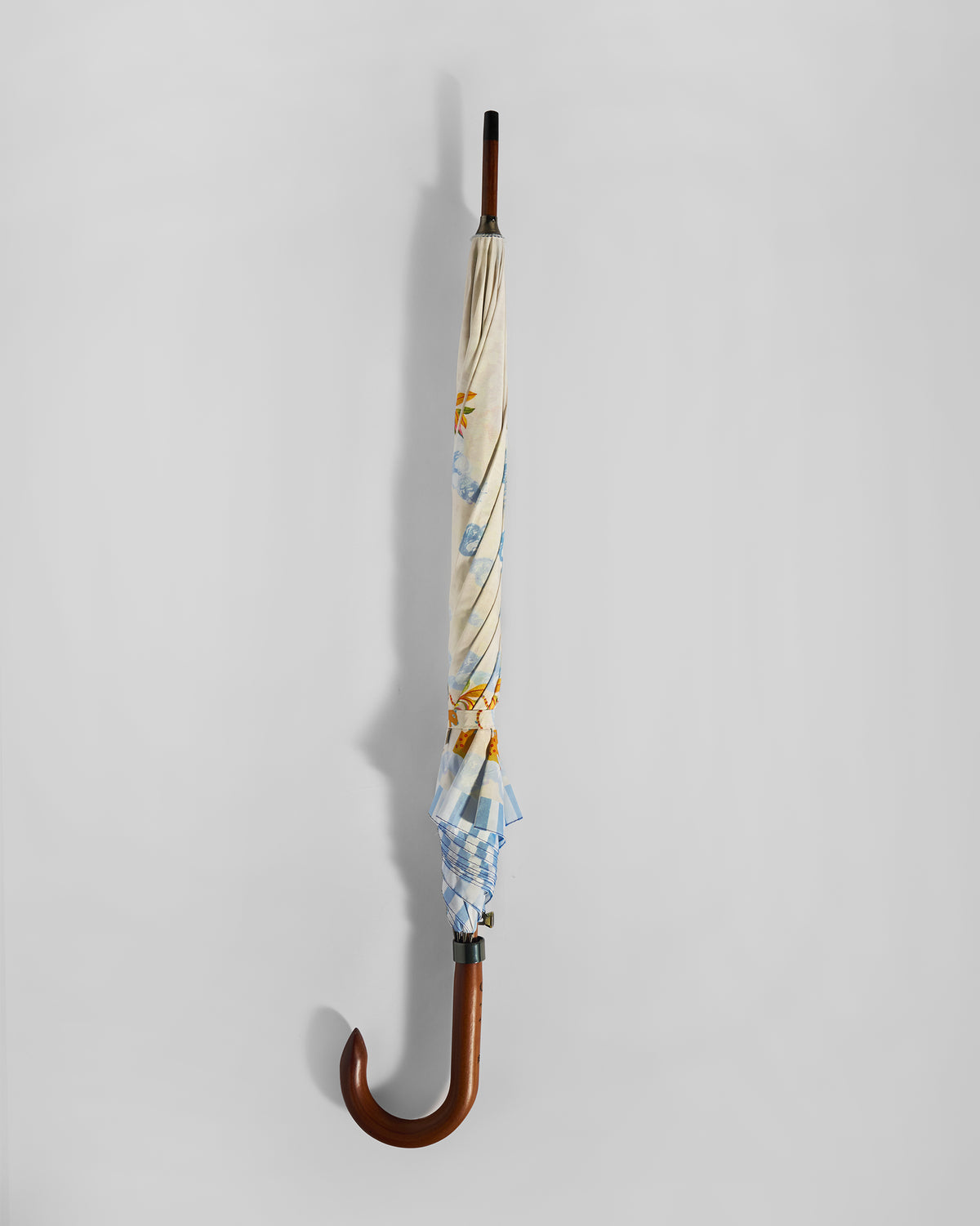 Closed Zanzibar Umbrella with a cream print and curved wooden handle.