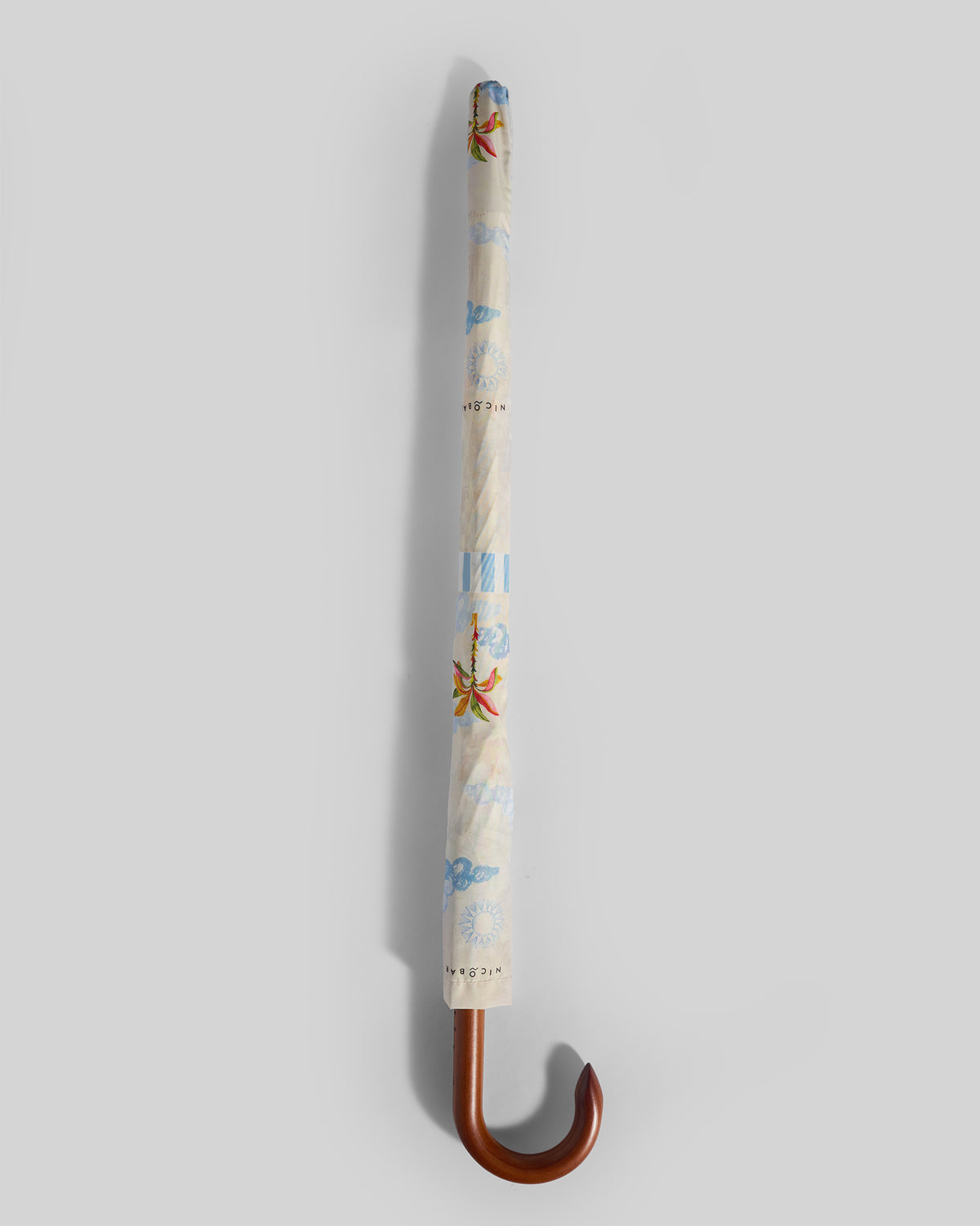 Furled Zanzibar Umbrella showing its cream cover, flower prints and curved handle.