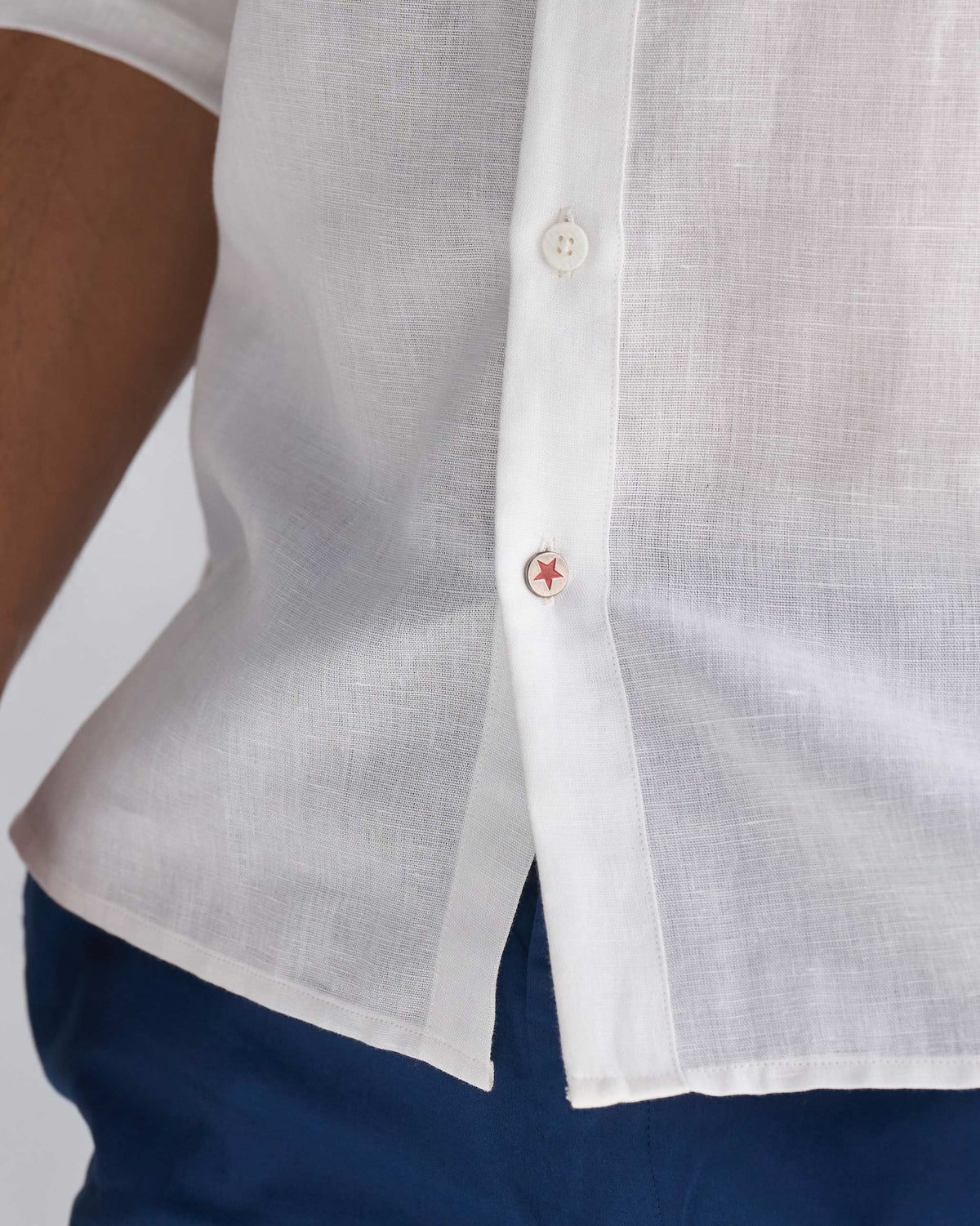 Close-up of a white August Shirt hem with a red star button at the side.