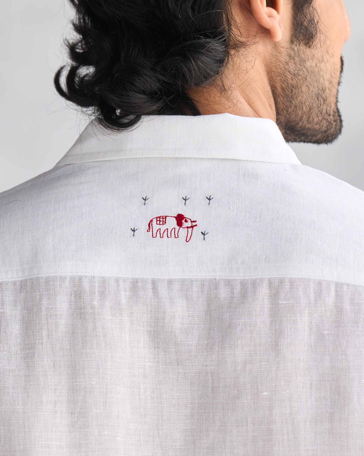 Back of a white August Shirt with a red embroidered elephant below the collar.