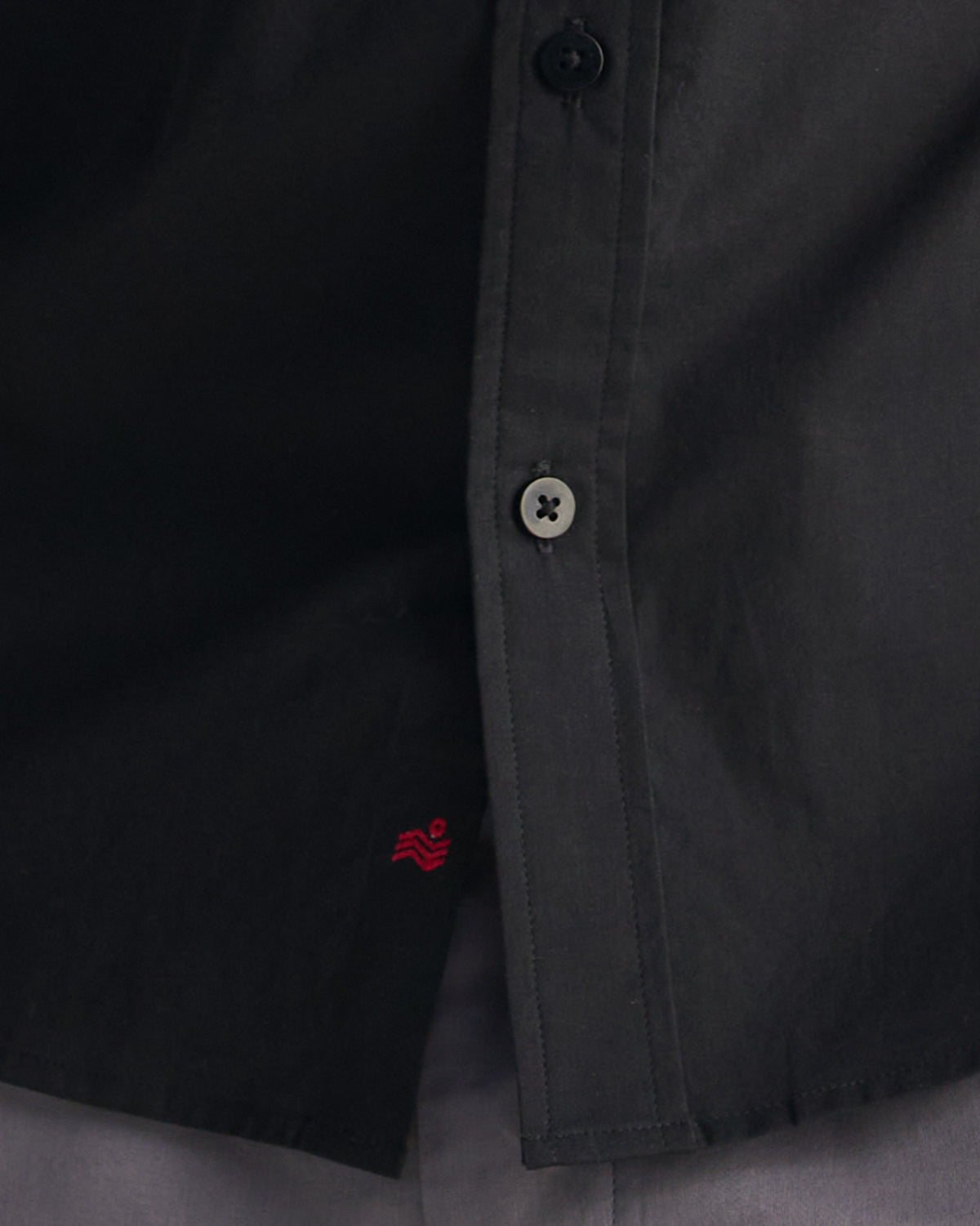 Close-up of black classic shirt hem with a small red wave mark.