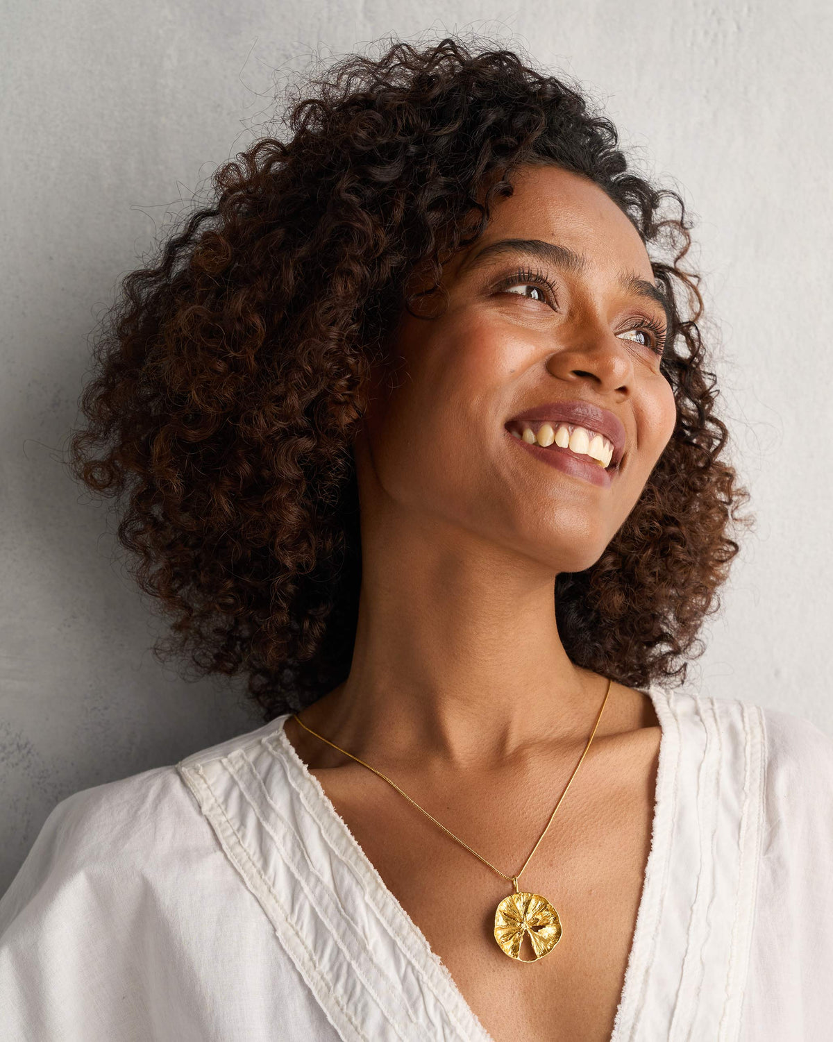 Person wearing a gold lemon slice charm on a thin chain.