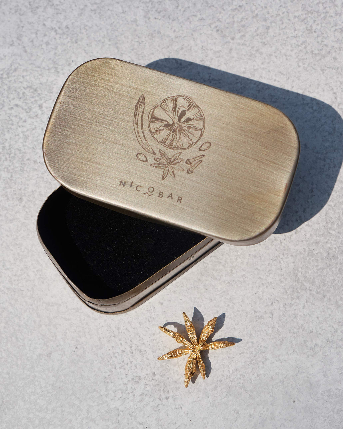Large gold Star Anise charm beside a Nicobar gift tin.