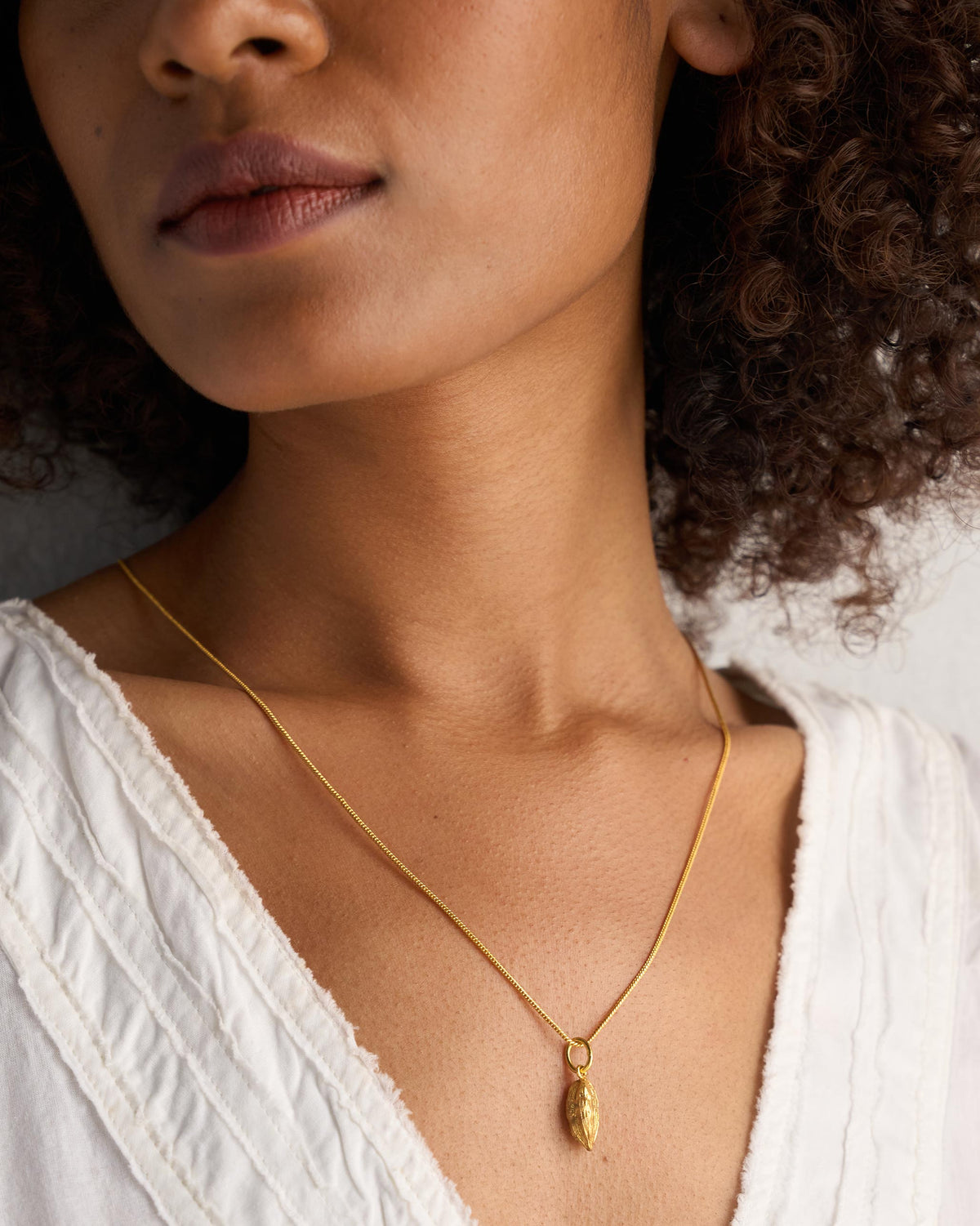 Small gold Cardamom charm worn as a pendant on a fine chain.