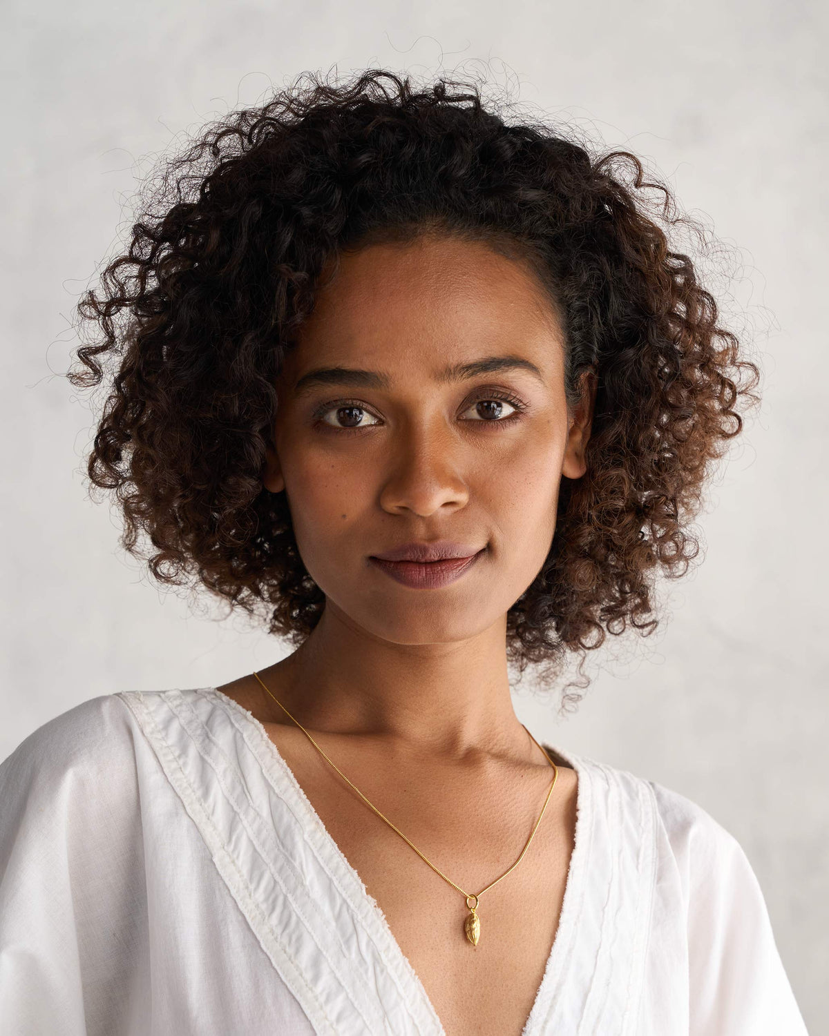 Person wearing a small gold Cardamom charm on a chain.