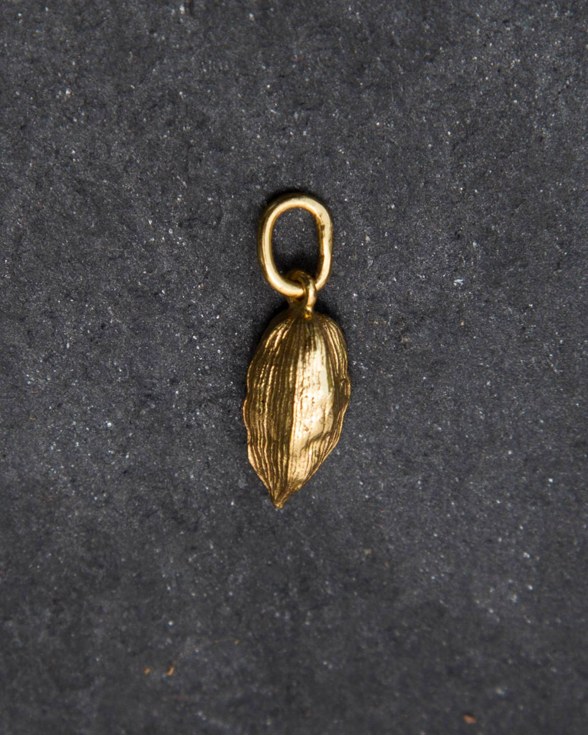 Close-up of a small gold Cardamom charm with ridged pod texture.