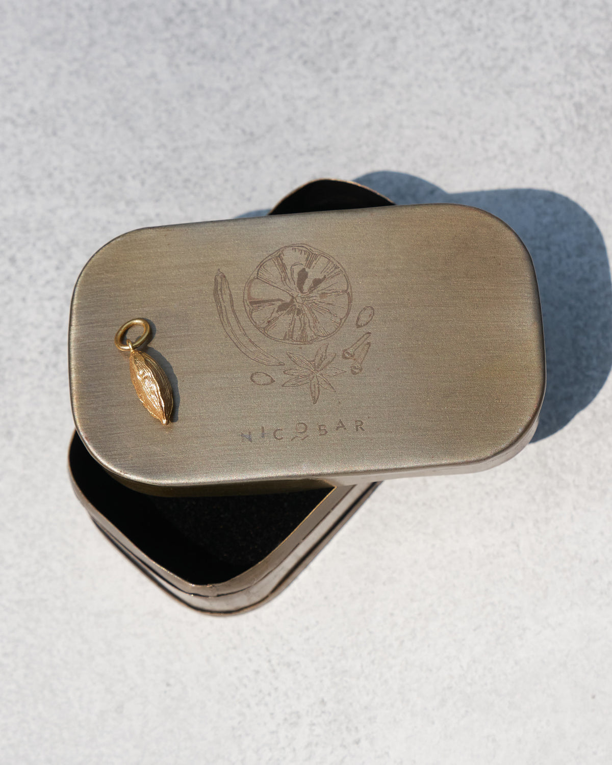 Gold Cardamom charm beside a Nicobar metal gift tin.