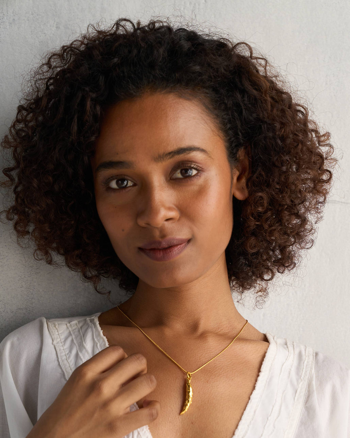 Person wearing a gold chilli charm on a thin chain.