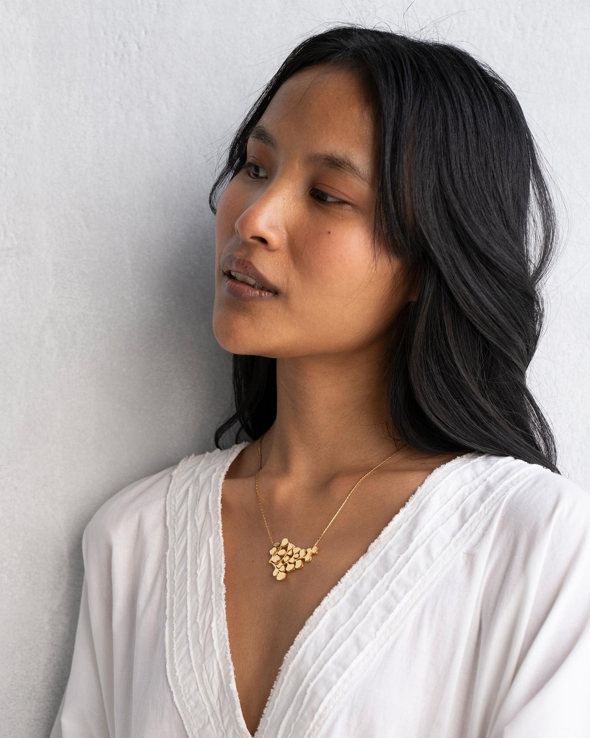 Person wearing a gold Fern Necklace with a cluster of leaves.