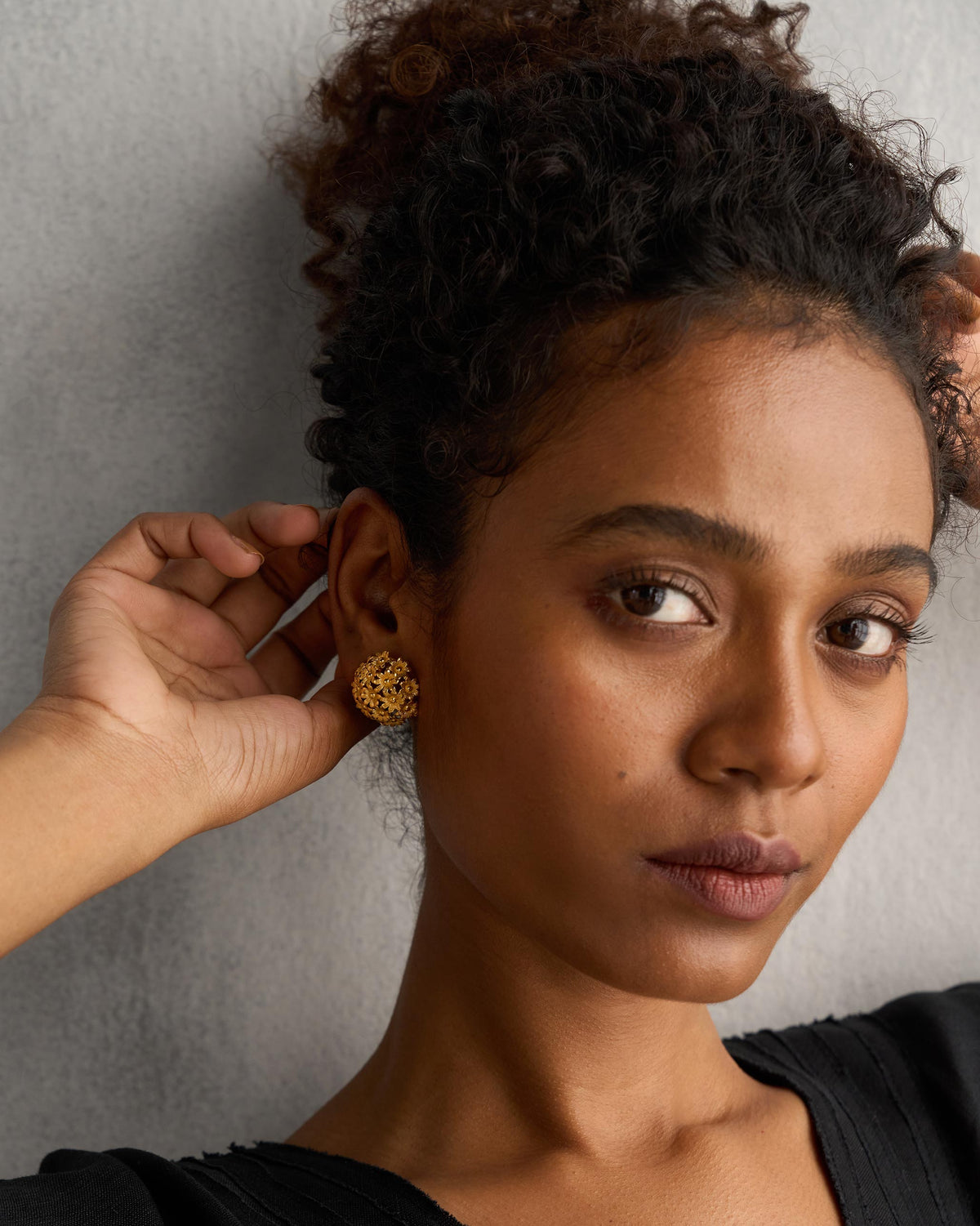 Person wearing a gold Rhododenron earring with a hand raised to the ear.