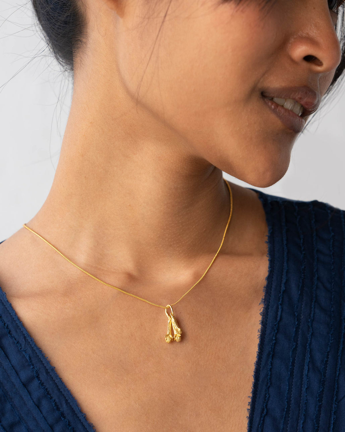 Gold snake chain with a clove pendant worn at the neck.
