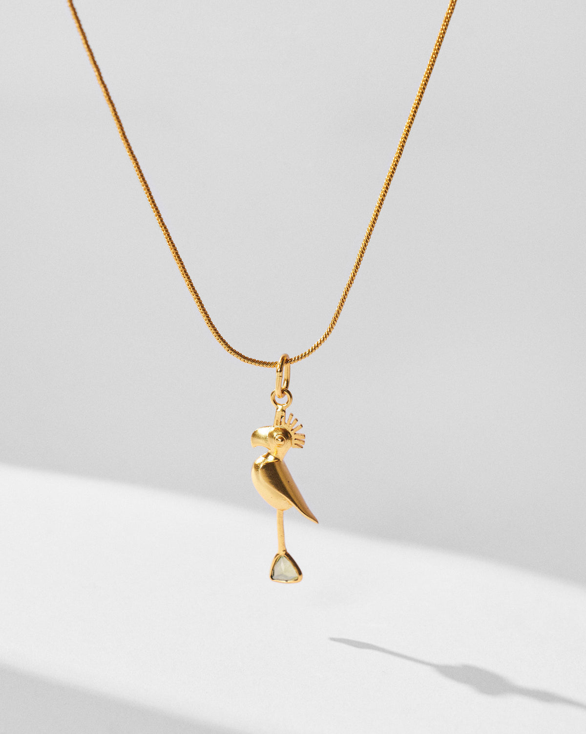 Gold Parrot Charm on a fine chain hung against a light background.