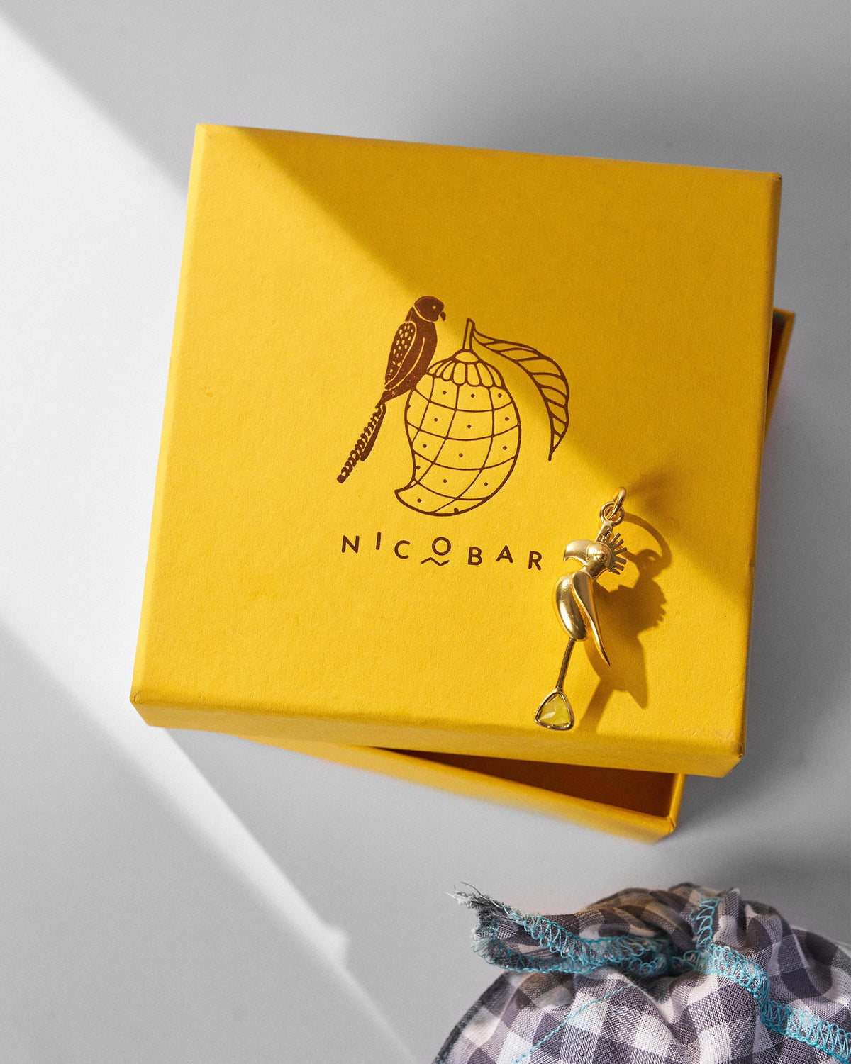 Gold Parrot Charm hanging beside a yellow Nicobar box.