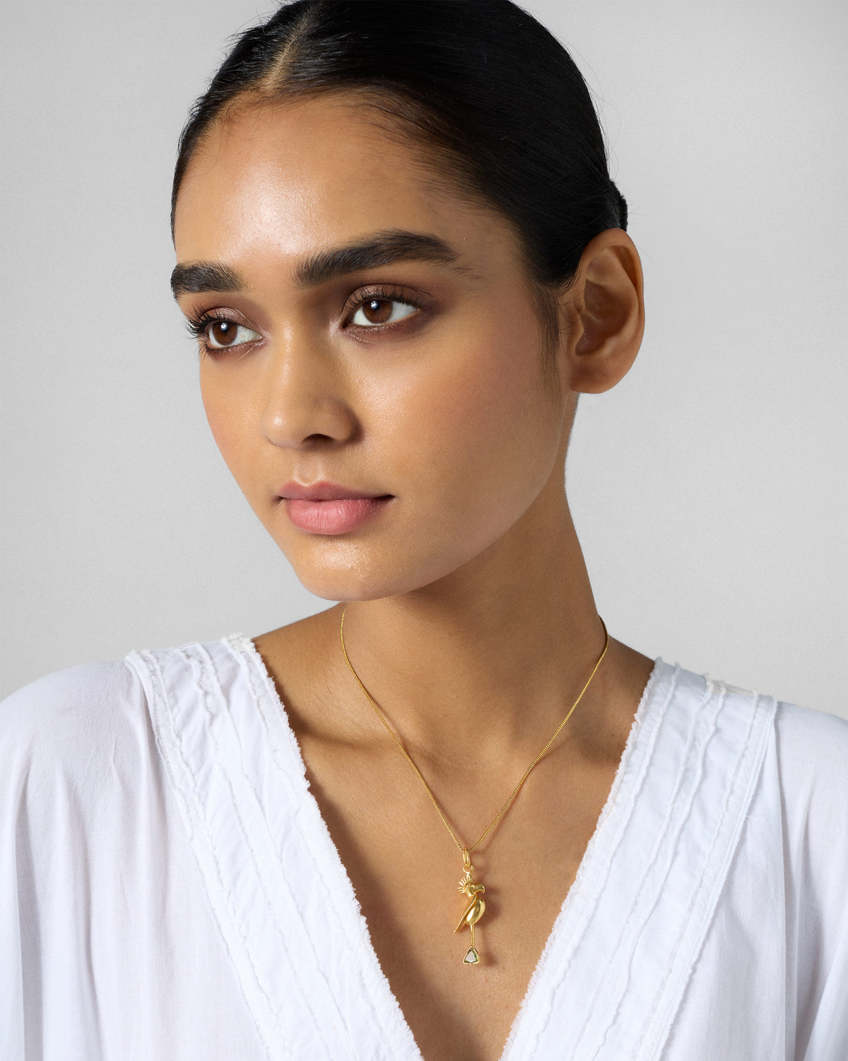 Person wearing a gold Parrot Charm on a fine chain, face turned to the side.