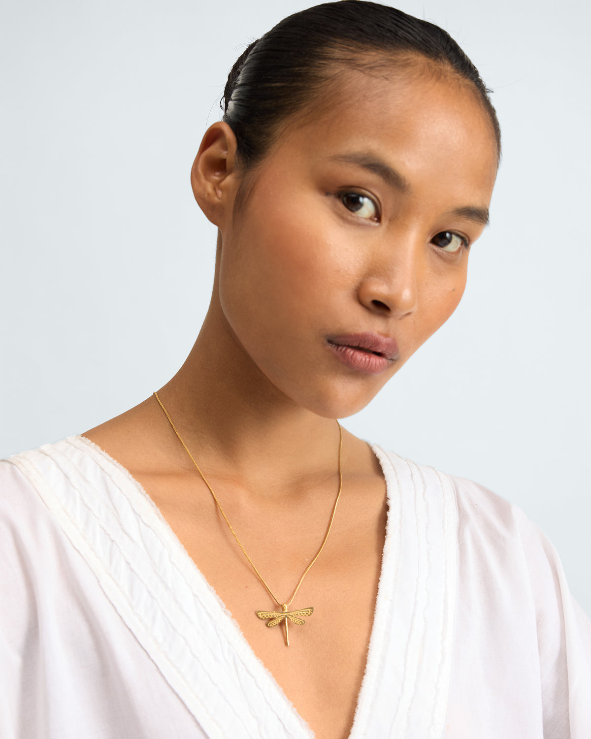 Upper body of a person wearing a gold Dragonfly Charm on a chain.