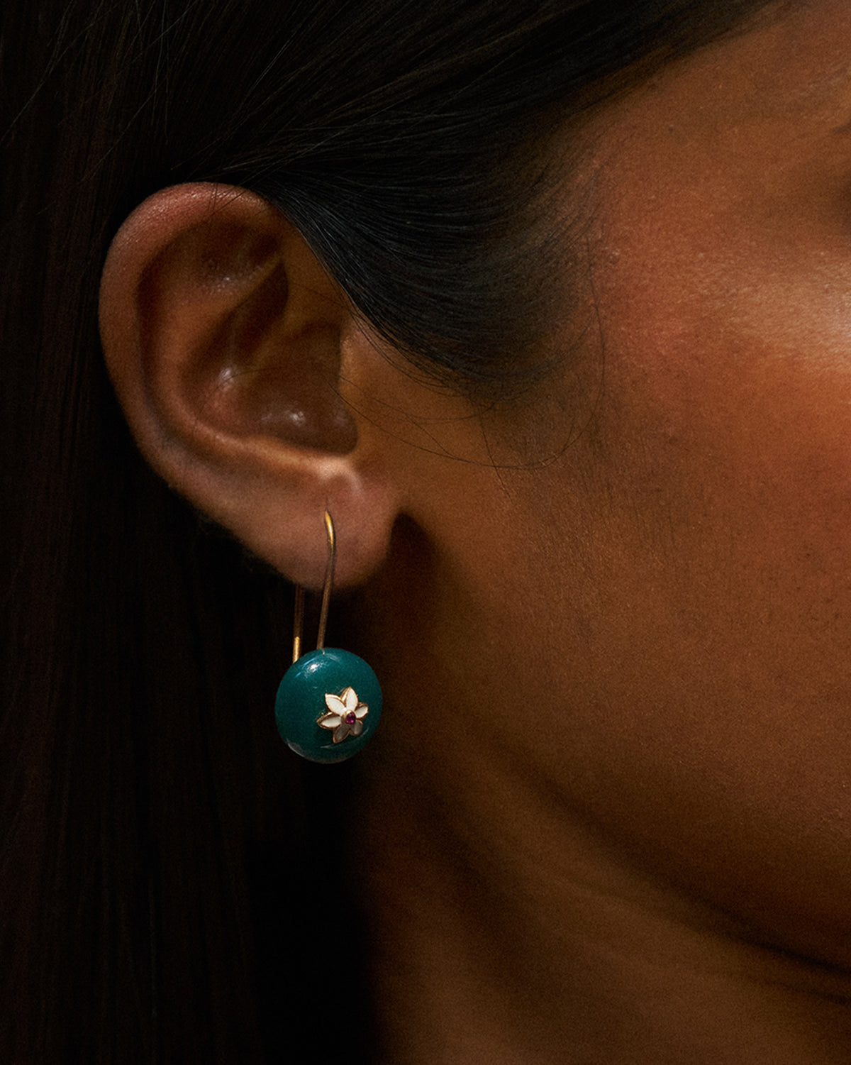 Close-up of a green onyx Aurora earring with a white flower motif.
