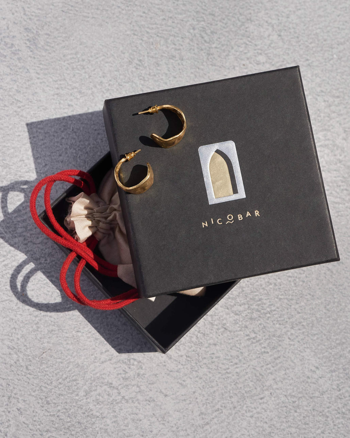 Pair of gold Seed Pod Small Hoops displayed on a Nicobar gift box.