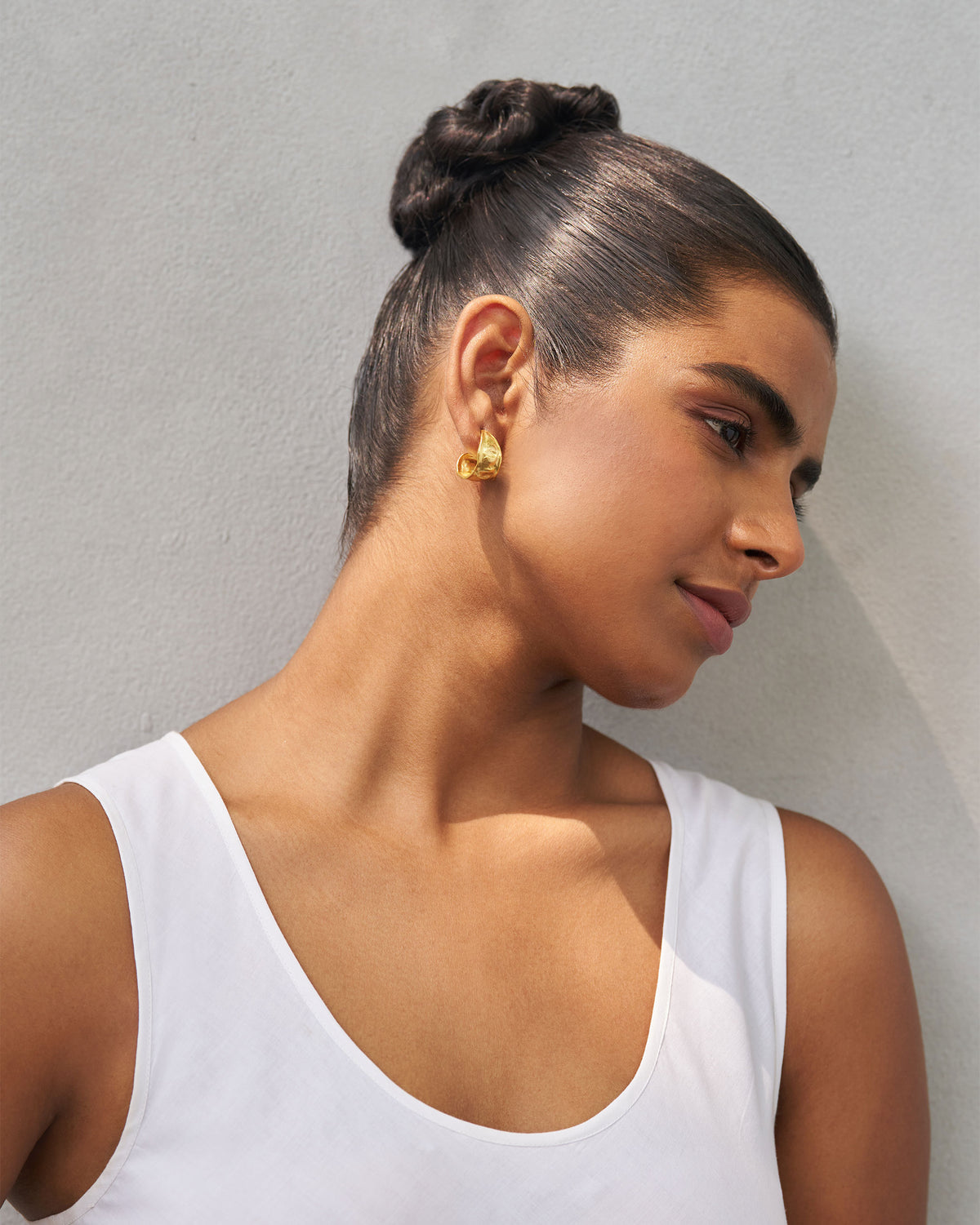 Person wearing gold Seed Pod Small Hoops, face turned to the side.