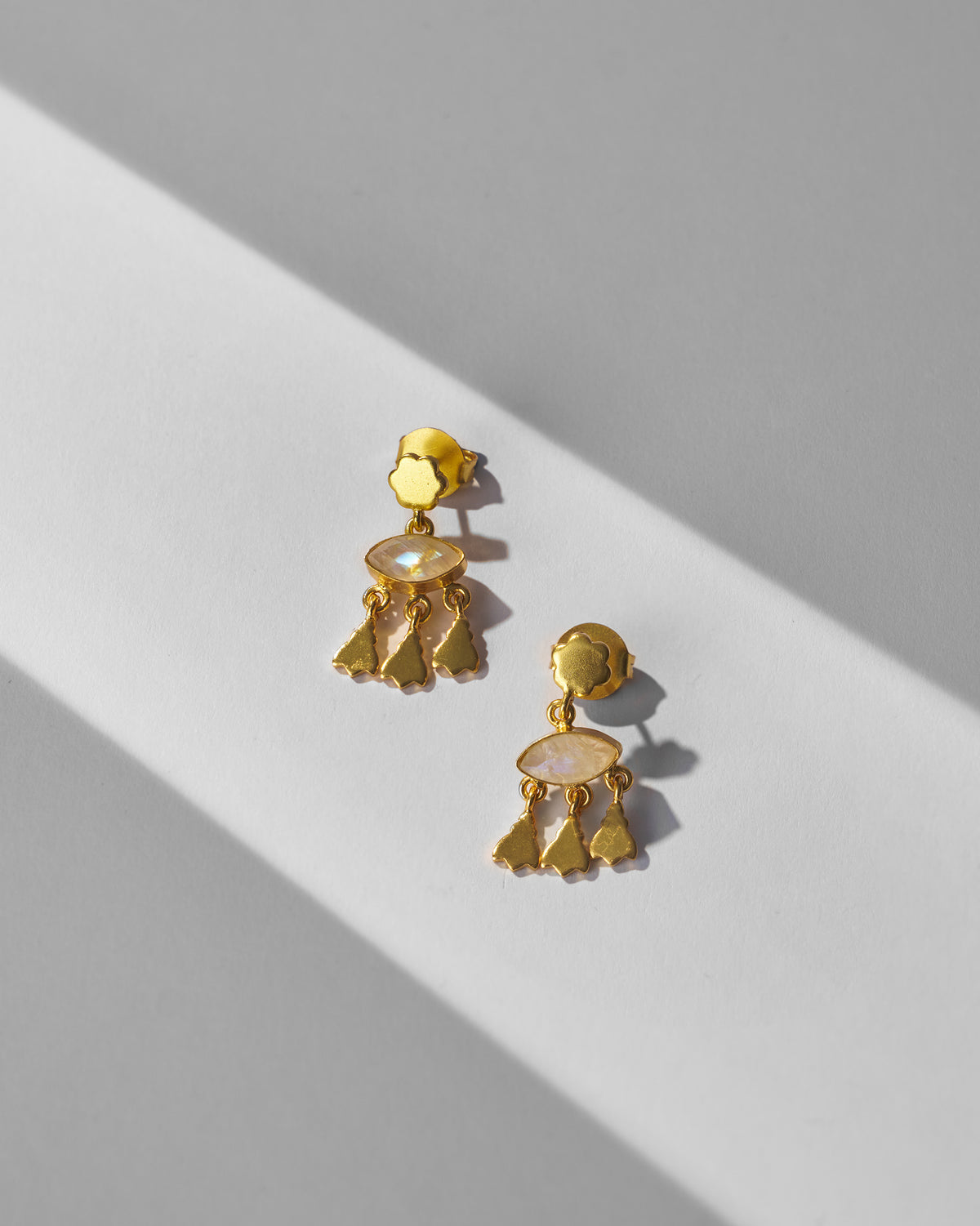 Pair of gold Jhalak earrings with moonstone drops laid flat.