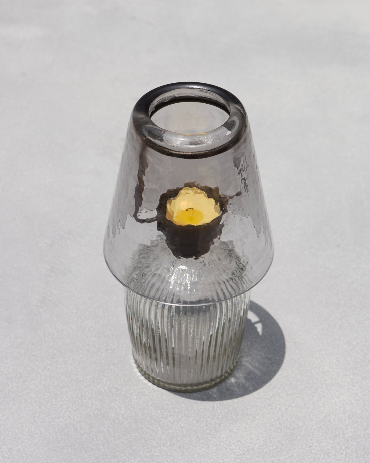 Lit Asfar votive glowing through a smoky glass shade on a ribbed base.