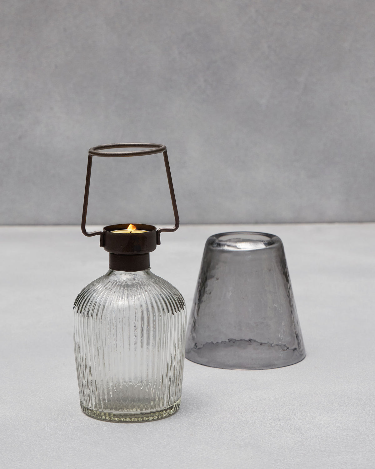 Asfar votive parts: lit tealight on a ribbed glass base beside the smoky shade.