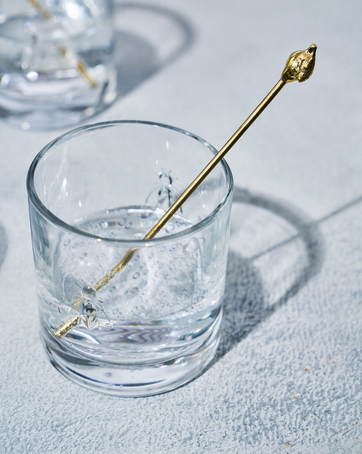 Clear Bumble Bee whiskey glass holding a gold cocktail stirrer.