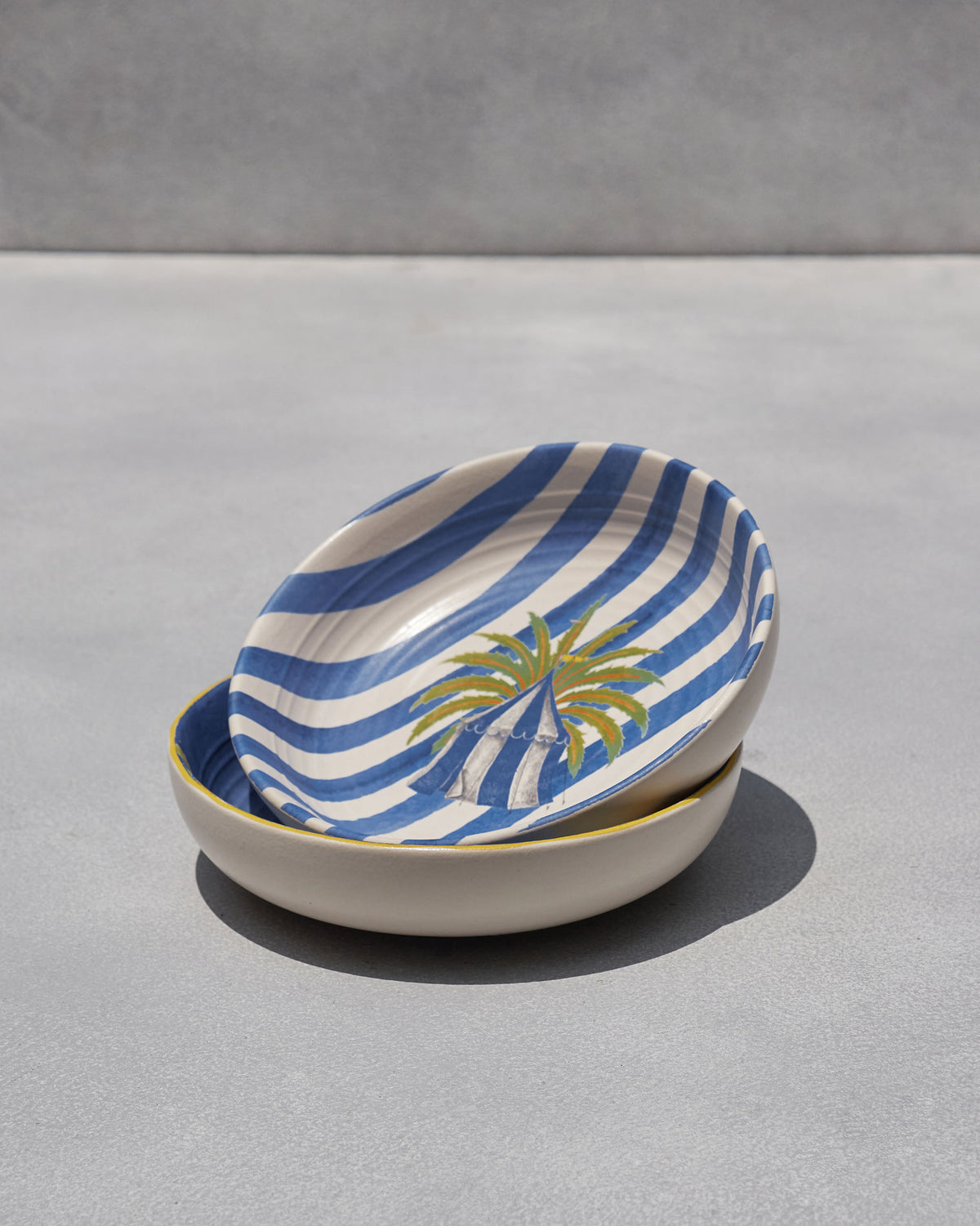 Sahara shallow bowl with blue-and-white stripes and a palm tent motif.