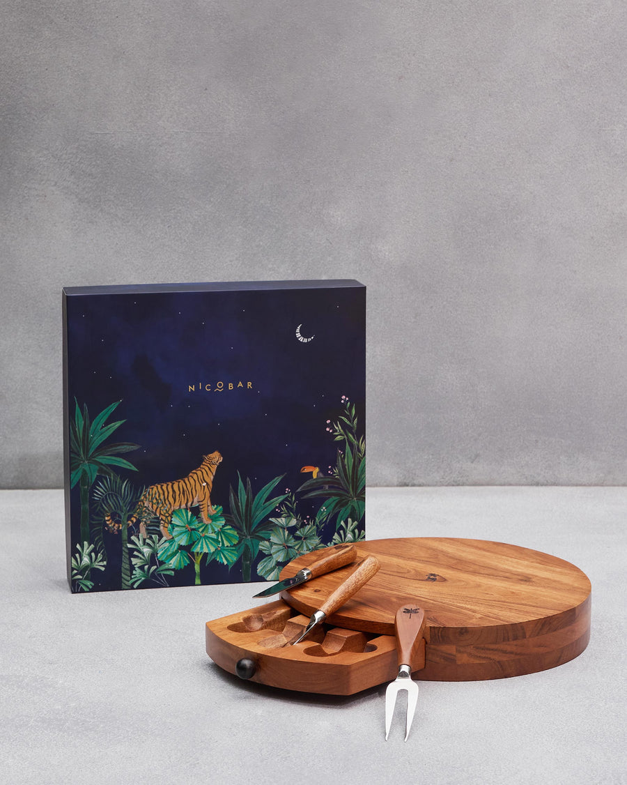 The round wooden Sahara board with its cheese knives beside the navy tiger box
