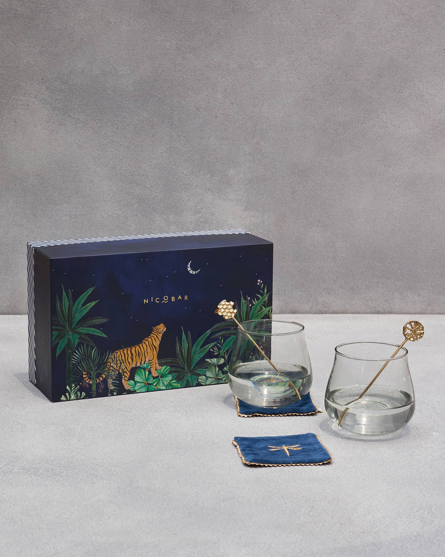 Azraq gin goblets with gold stirrers and navy coasters beside the tiger box